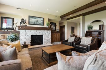 A cozy living room at Silver Star 1303 features a stone fireplace, plush sofas, leather armchairs, and a wooden coffee table, all under ambient lighting.