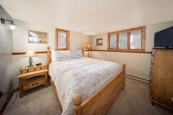The bedroom features a wooden bed frame, a patterned comforter, a nightstand with a lamp, and a dresser with a TV.