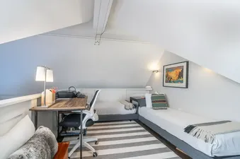 A cozy loft bedroom at The Hummingbird House with two single beds, a wooden desk, and a striped rug, all bathed in soft lighting.