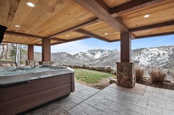 An outdoor hot tub with bubbling water on a tiled patio, set against a backdrop of snow-capped mountains under a clear blue sky.