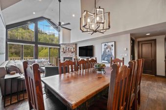 A spacious dining area at St James Place 437 with a large wooden table and chairs, featuring a view of lush mountains through grand windows.