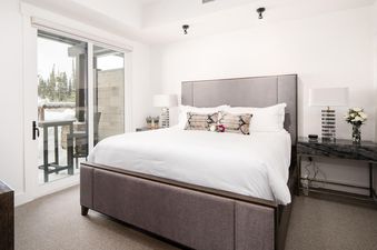 The plush bed in the bedroom at Moonlight Basin 9 Wildwood boasts crisp white linens and a plush grey headboard. The windows open onto a stunning view of the winter wonderland outside.