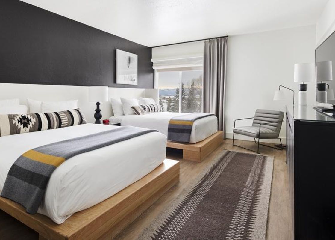 Modern hotel room with two queen beds, a sleek accent wall, and a comfortable armchair by the window.