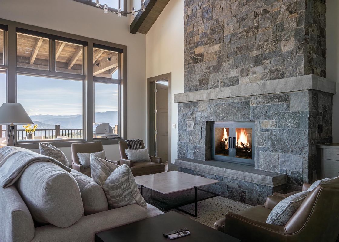 The spacious living room of Inspiration Point Townhome 14A features a large stone fireplace, plush seating, and expansive windows offering stunning mountain views.