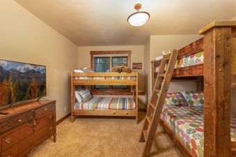 A cozy bunk room in Bear Tracks Lodge with two wooden bunk beds, a television displaying a fall landscape, and warm lighting.