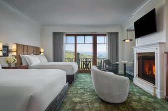 A luxurious bedroom featuring two queen-sized beds, a cozy fireplace, and a private balcony overlooking a scenic mountain landscape.