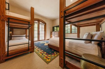 A bunk room at Four Bears Hideaway at See Forever features sturdy wooden bunk beds, a colorful geometric rug, and arched doors leading to an outdoor view.