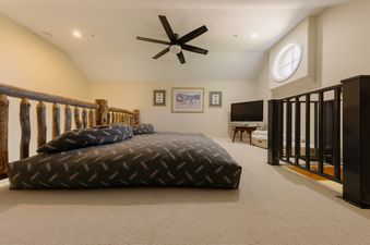 A cozy loft bedroom in Crystal Ridge featuring a low-profile bed, circular window, and log railing.