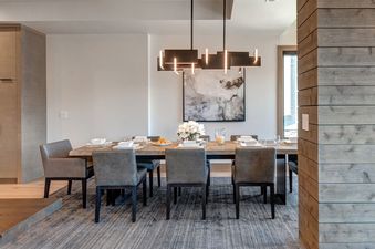 The dining area at Abode at Powder King features a wooden table with seating for eight, a modern chandelier, and abstract art, all set against light-colored walls and a textured rug.