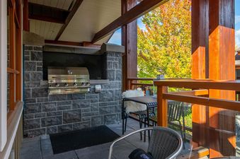 A covered balcony with a built-in stone barbecue, dining table, and views of autumn trees.