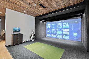 A modern game room featuring a large 'Full Swing' golf simulator screen, a console with a monitor, a golf bag, and sports balls.