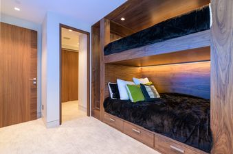 A modern bunk bedroom featuring custom wood built-in beds with black bedding.