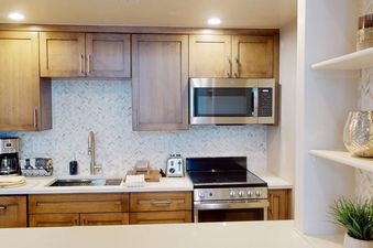 A kitchen with stainless steel appliances, wooden cabinets, and a white tile backsplash.