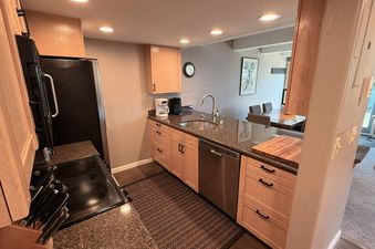 A modern kitchen in Vail International 002 features a black stove, black refrigerator, and wood cabinets, with a granite countertop and stainless steel dishwasher.