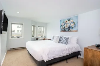 A serene bedroom at Lulu Luxe with a queen-sized bed, floral painting, wooden nightstand with a lamp, and a wall-mounted TV.