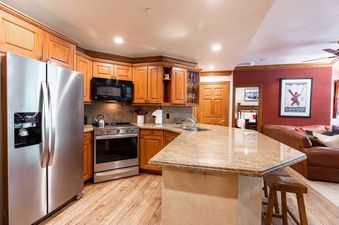 A kitchen with stainless steel appliances, wooden cabinets, a granite countertop, and a bar with two stools.