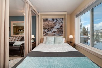 The Snowblaze E102 has a cozy bedroom area with a large mural above the bed and a window offering a beautiful snow-covered mountain view.