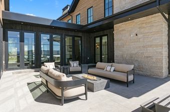 An outdoor patio at SkyRidge 1843 featuring modern sofas, a stone accent wall, and a central fire pit table under a clear blue sky.