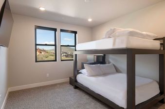 A modern bedroom at Retreat at Jordanelle with a bunk bed, a wall-mounted TV, and two large windows offering a view of surrounding houses and mountains.