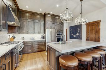 A modern rustic kitchen featuring dark wood cabinetry, stainless steel appliances, a large island with a sink and bar stools, and two stylish pendant lights.