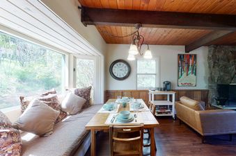 A dining area at Cozy Condo on Chamonix Lane with a wooden table, bench seating by a large window, a leather sofa, and a stone fireplace.