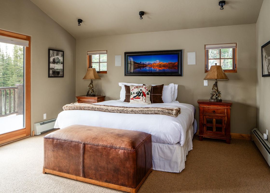 The master bedroom at Moonlight Basin 2 Mountain Home features a large, comfortable bed with a furry throw and a window with a view of the trees outside.