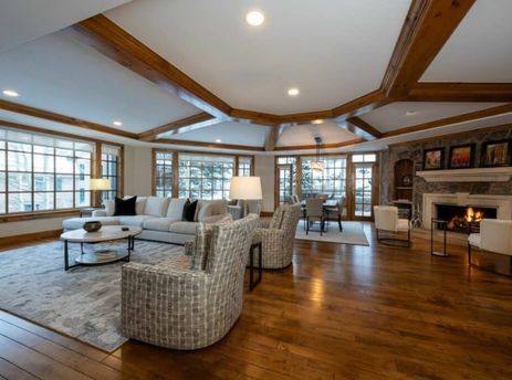 The Chateau Beaver Creek Residence 306's open-concept living and dining area features rich hardwood floors, exposed wooden beams, a comfortable living room with a stone fireplace, and a dining space with large windows overlooking a winter landscape.