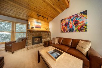 The living area at Creekside 403 features a comfortable brown leather sectional sofa and a stone fireplace.