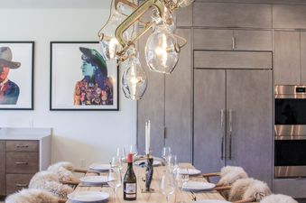 A rustic-chic dining room in Hidden Hollow 304 featuring a unique chandelier made of chains and clamps, a live-edge wooden table, and chairs with sheepskin throws, set for a meal.