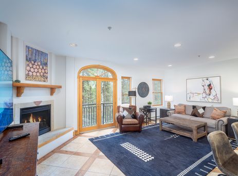 The living room in Bear Creek Lodge 202 features a fireplace, a leather armchair, a couch, a coffee table, a rug, and a view out of a french door