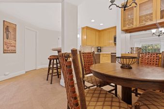 A cozy dining area and kitchenette inside The Charter B3305, featuring a round wooden table with rustic chairs, a bar with stools, and light wood cabinetry.