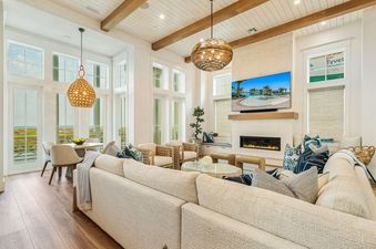 The Palmilla Pearl living area features a large L-shaped sofa, a dining area, a flat-screen TV above a fireplace, and large windows with outdoor views.