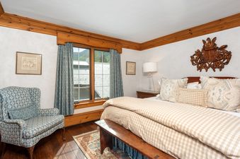 The Chateau Christian 2 Bedroom Platinum Unit 310 features a cozy bedroom with a large bed, an armchair, and a window offering a view of the mountains and the surrounding buildings.