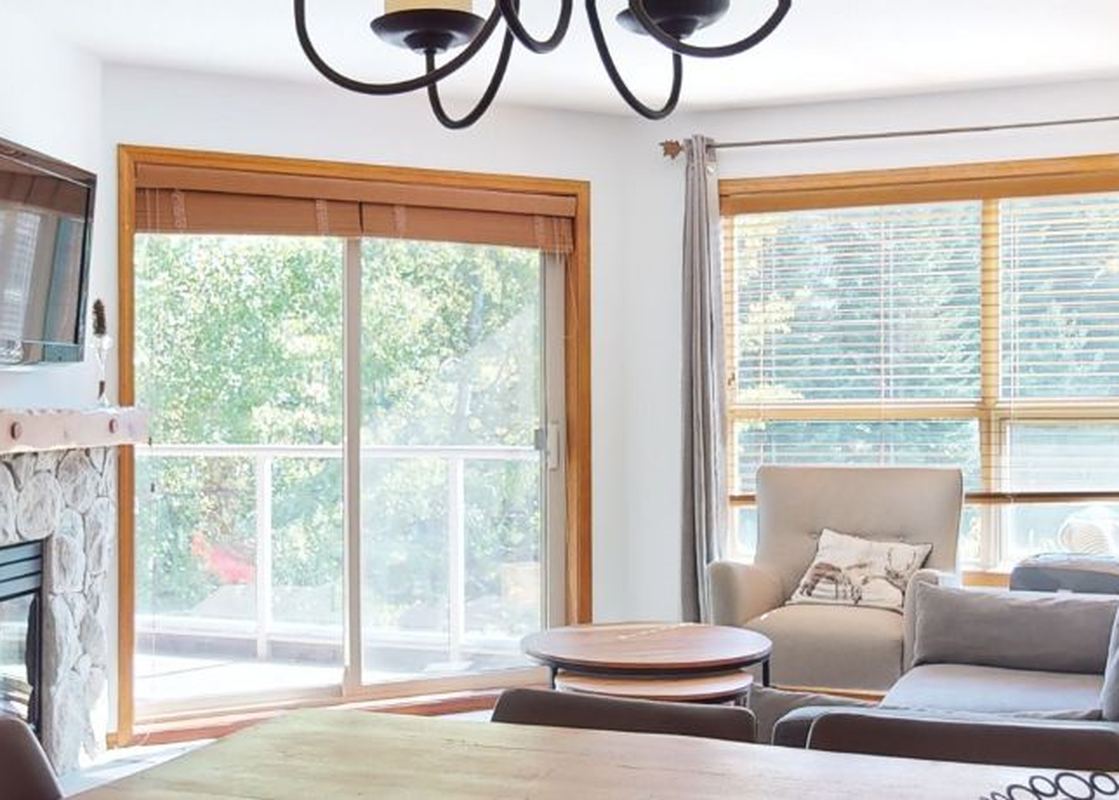 A cozy living room at Aspens on Blackcomb Unit 332 features a stone fireplace, mounted TV, and large windows leading to an exterior view.