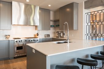 A modern kitchen with light gray cabinetry, white countertops, stainless steel appliances, and a kitchen island with bar stools at Silver Star 41DX.