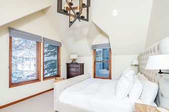 A bedroom with a king-sized bed, a large window, and a dresser with a lamp on top.