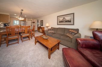 The living area within Beaver Village 1123 features an open-concept design, connecting the comfortable living room, the rustic dining area, and the functional kitchen, all bathed in natural light.