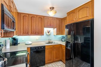 The image shows a full view of the kitchen in the All Seasons 2 Bedroom Gold Unit G3, featuring wooden cabinetry, modern appliances, and light blue walls.