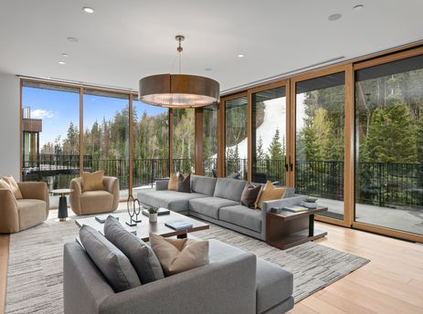 A luxurious living room at Founders Place 1504 with a large grey sectional sofa, two beige armchairs, and floor-to-ceiling windows revealing a mountain landscape.