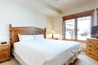 EagleRidge Lodge 300 master bedroom with a king-size bed, nightstands, a dresser, a flat-screen TV, and a window with a view of the snowy mountains