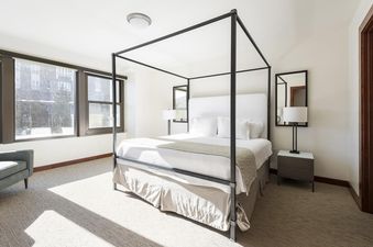 A bedroom with a four-poster bed and a window with a view of a snow-covered landscape outside.