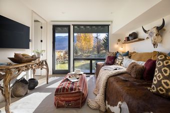 The lounge area in Hidden Hollow 304 features a daybed with a cowhide throw, a rustic console, and large windows overlooking autumn mountains.