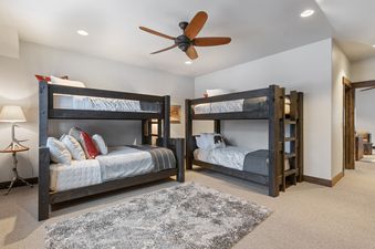 A spacious bunk room with two dark wood bunk beds, plush bedding, a patterned gray rug, and rustic decor, designed for comfortable group stays.