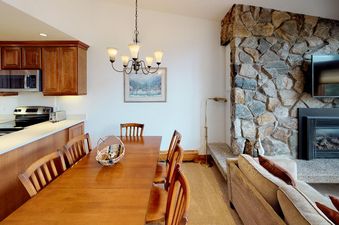 The dining area of Manor Vail 348 has a wooden table with four chairs, a chandelier hanging from the ceiling, and a picture hanging on the wall.