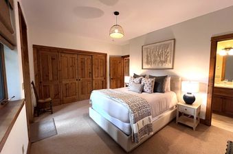 A serene bedroom at Bear Lodge with a queen bed, wooden closet doors, and a bedside table with a lamp.