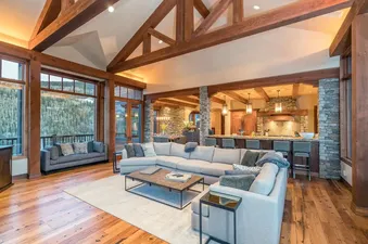 The spacious living room in Two Trails is open and inviting with a large sectional sofa centered in the room, floor-to-ceiling windows, and a wood-beam ceiling.