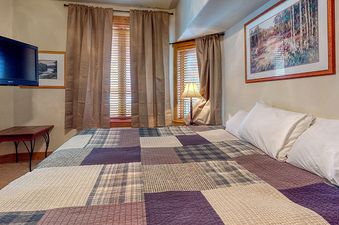 The bedroom in EagleRidge Lodge 211 features a unique vaulted ceiling with a patchwork quilt.  The room has two windows with blinds, and a large artwork on the wall.