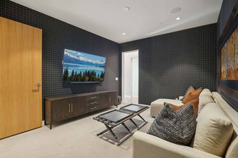 A modern media room at Founders Place 2303 with dark paneled walls, a large wall-mounted TV, a dark wood credenza, and comfortable seating with decorative pillows.