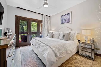A luxurious bedroom at The Charter D3505 featuring a large bed with decorative pillows, mirrored nightstands, a stylish dresser, and French doors leading to a balcony with green views.