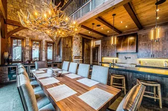 A rustic dining room with a large wooden table, chairs, and a chandelier made of antlers.